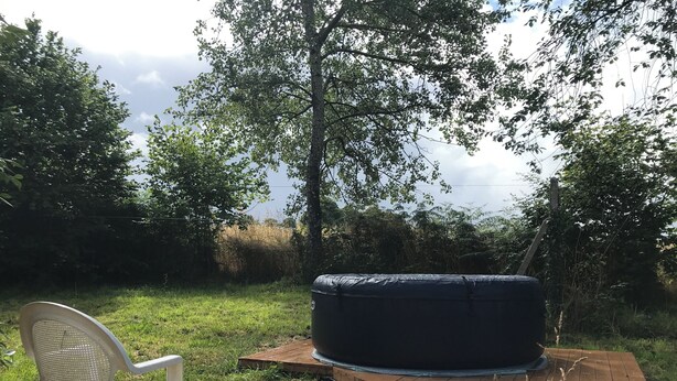 Una terrazza in legno con una zona relax rotonda nera e una sedia in plastica bianca.