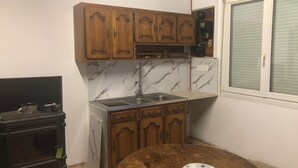 Una cucina compatta con mobili in legno, uno schienale in marmo, un lavello e un piccolo tavolo rotondo con sottotavolo floreale.
