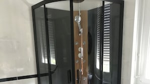 Una camera d'angolo con cabina doccia in vetro, pavimento in legno e finestra con persiane.