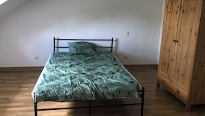 Un letto singolo con copriletto a motivi fogliari in una stanza con pavimento in legno, soffitto spiovente e armadio in legno.