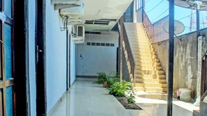 Un pasillo estrecho con una escalera que sube a un nivel superior. Se observan unidades de aire acondicionado en las paredes, y un plato parabólico a la derecha.