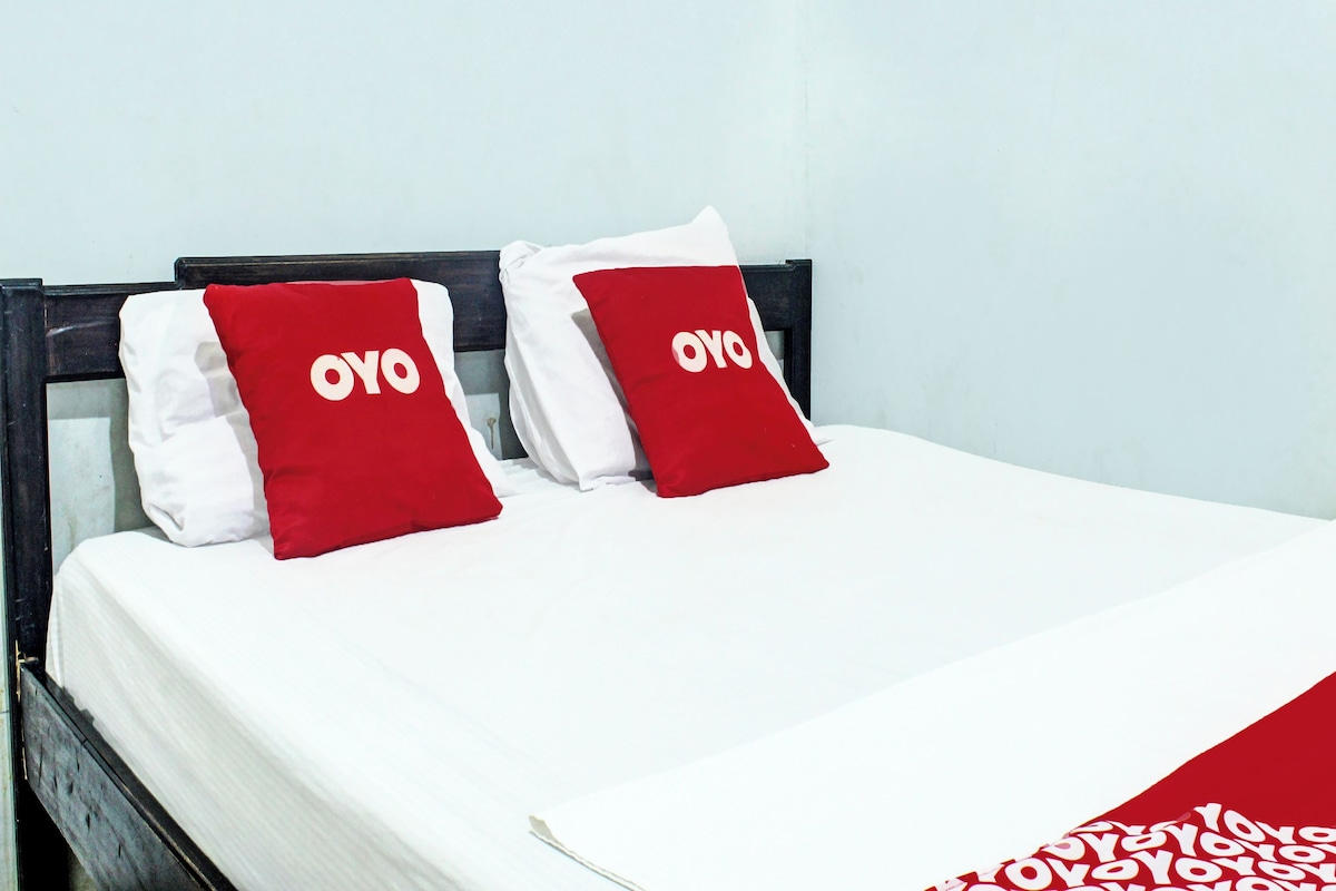 A bed with white bedding and two red pillows with the word "OYO" on them.
