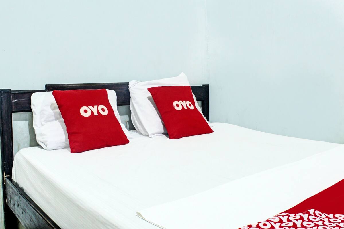 Una cama con ropa de cama blanca y dos almohadas rojas con el texto "OYO".