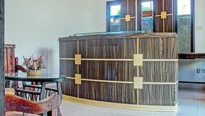 Un mostrador de recepción con acabado similar al mármol, una mesa de vidrio y sillas de madera.