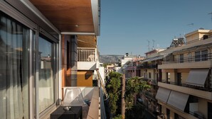 A balcony with a table and chairs, a view of neighboring buildings, and a clear sky. - The Luxury Loft by Cloudkeys (Athens)