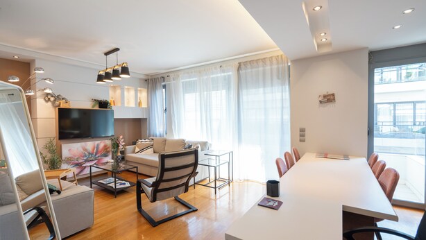 A modern living room with a flat-screen TV, a sofa, a coffee table, and a dining area with a long table and chairs. - The Luxury Loft by Cloudkeys (Athens)