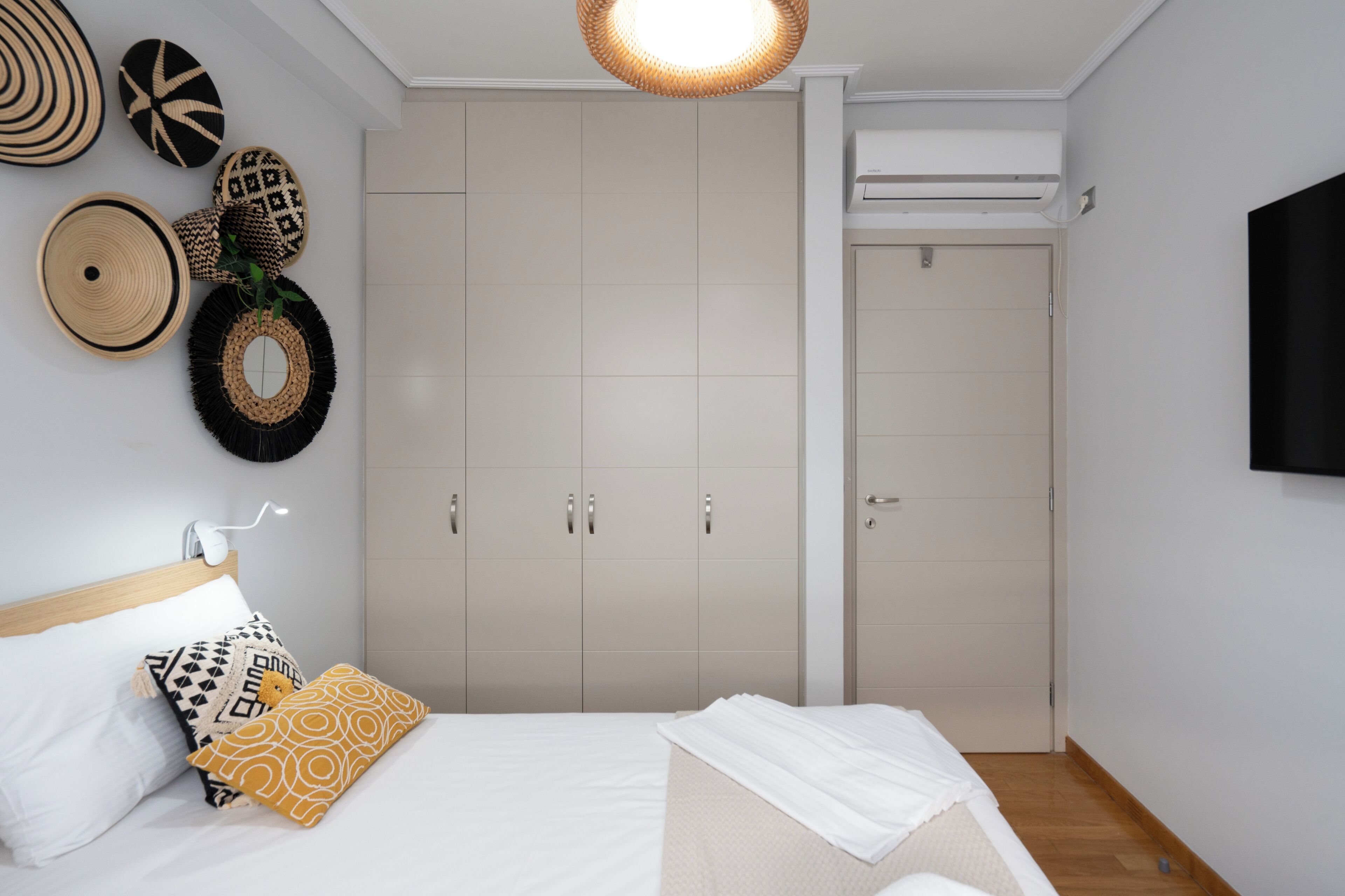 A bedroom with a bed, a wardrobe, a wall-mounted TV, and decorative wall hangings.