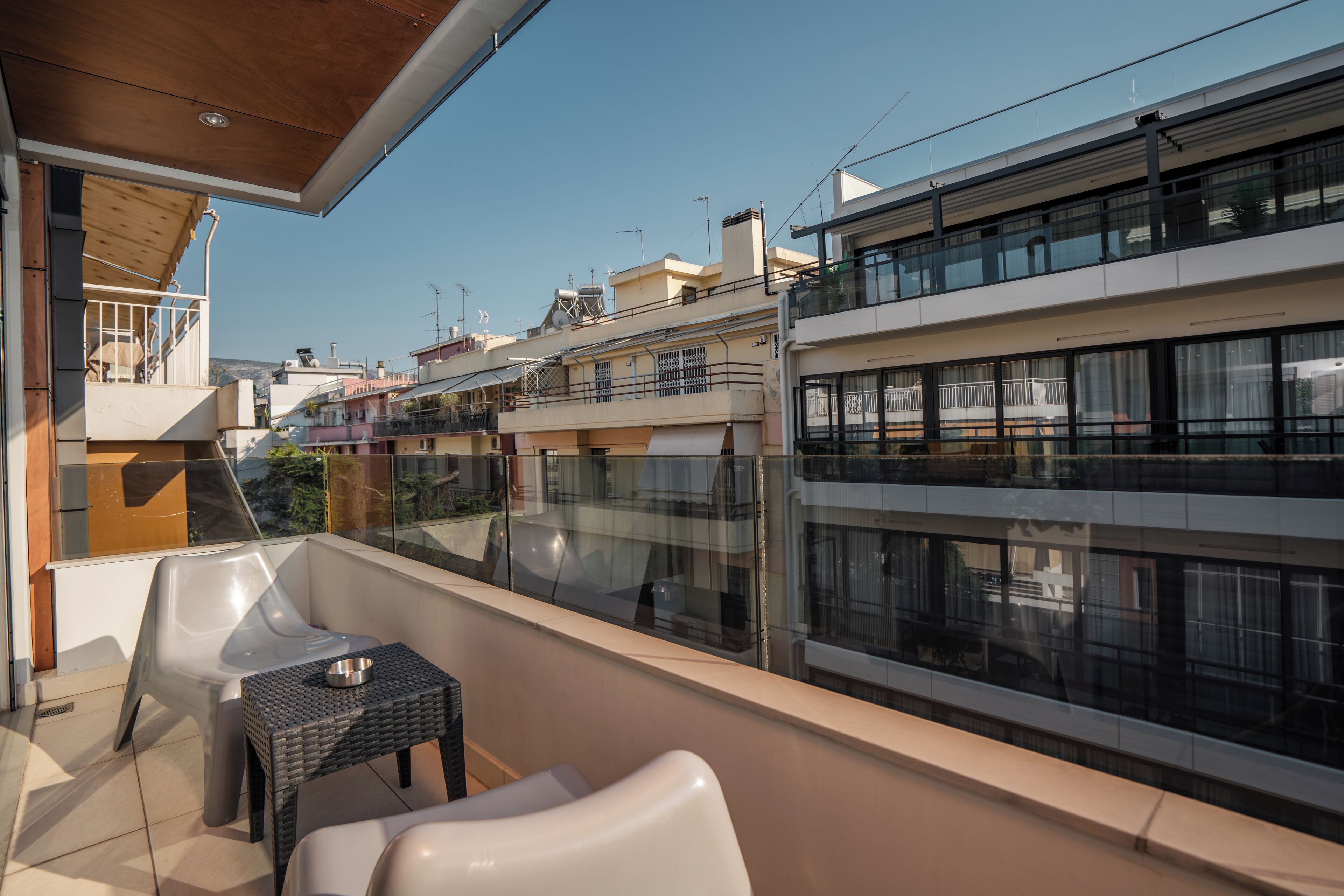 A balcony with a wicker table and two chairs, overlooking a residential area with modern buildings.