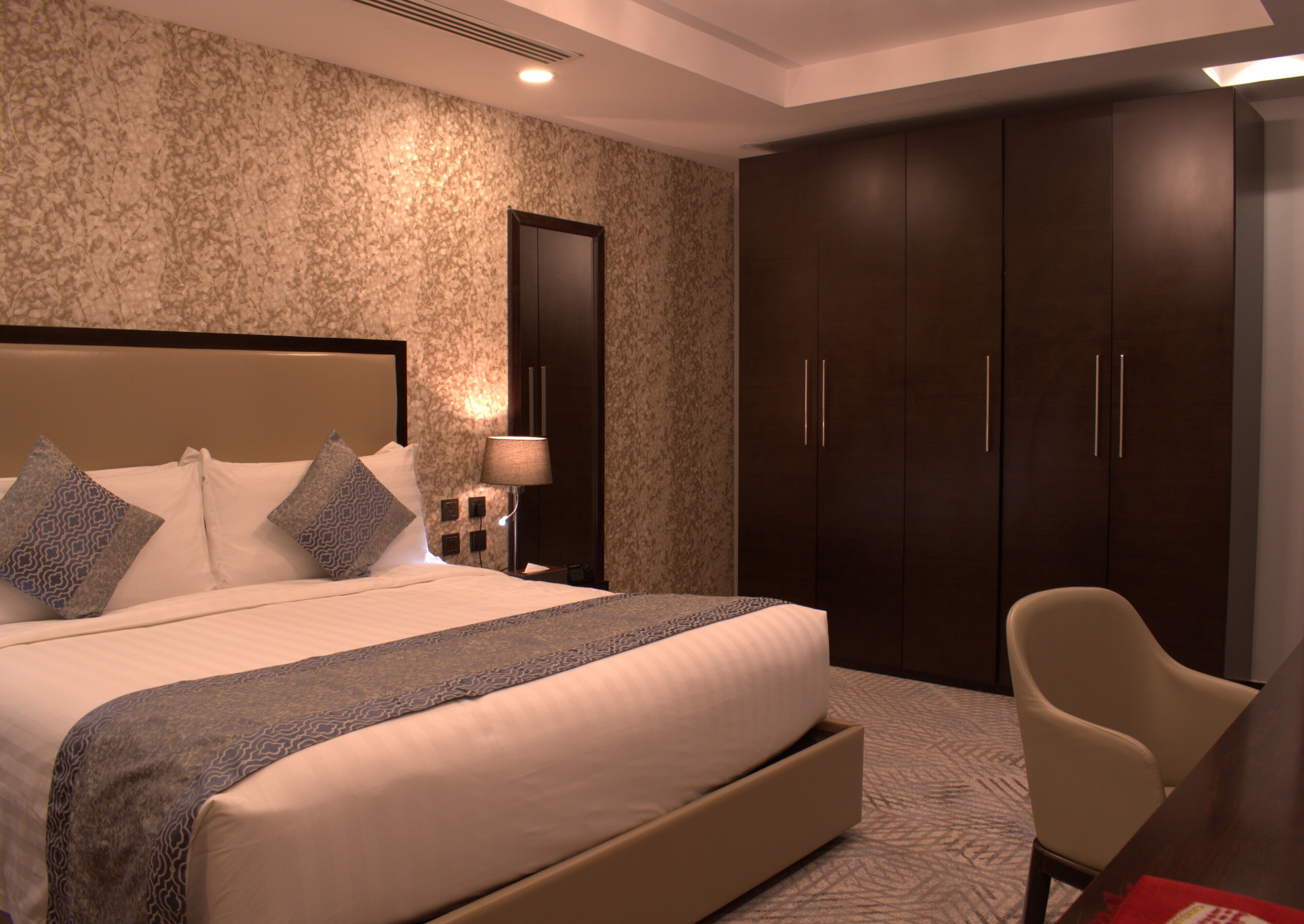 Quarto de hotel moderno com uma cama grande, mesa de cabeceira, escrivaninha e guarda-roupa.