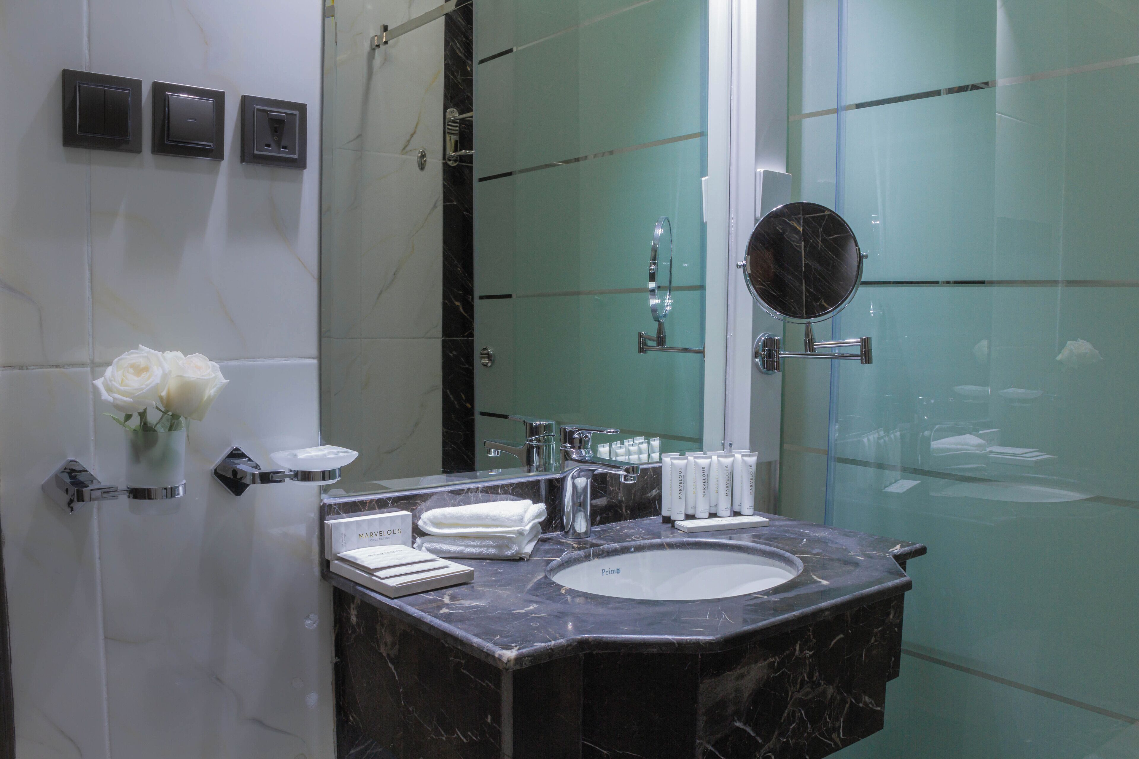A modern bathroom with a marble sink, a large mirror, and a vase of white roses.