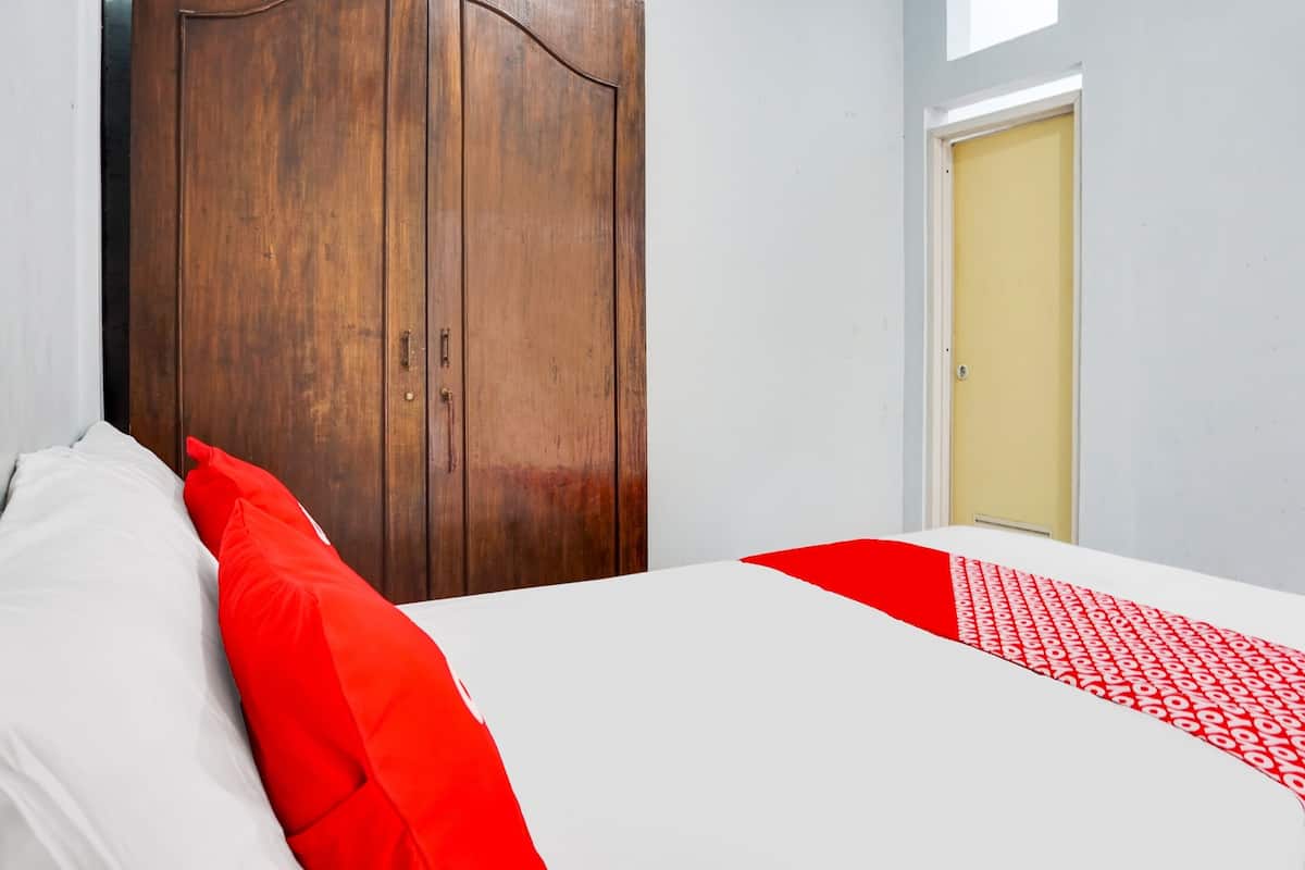 Un dormitorio con un armario de madera, una cama con ropa de cama blanca y roja, y una puerta amarilla.