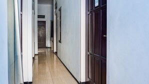 Un pasillo con piso de baldosas, una puerta con el signo de número y una ventana a la izquierda.