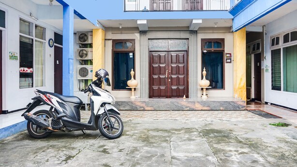 Un edificio de dos plantas con una entrada central, una moto estacionada adelante y un pequeño jardín.