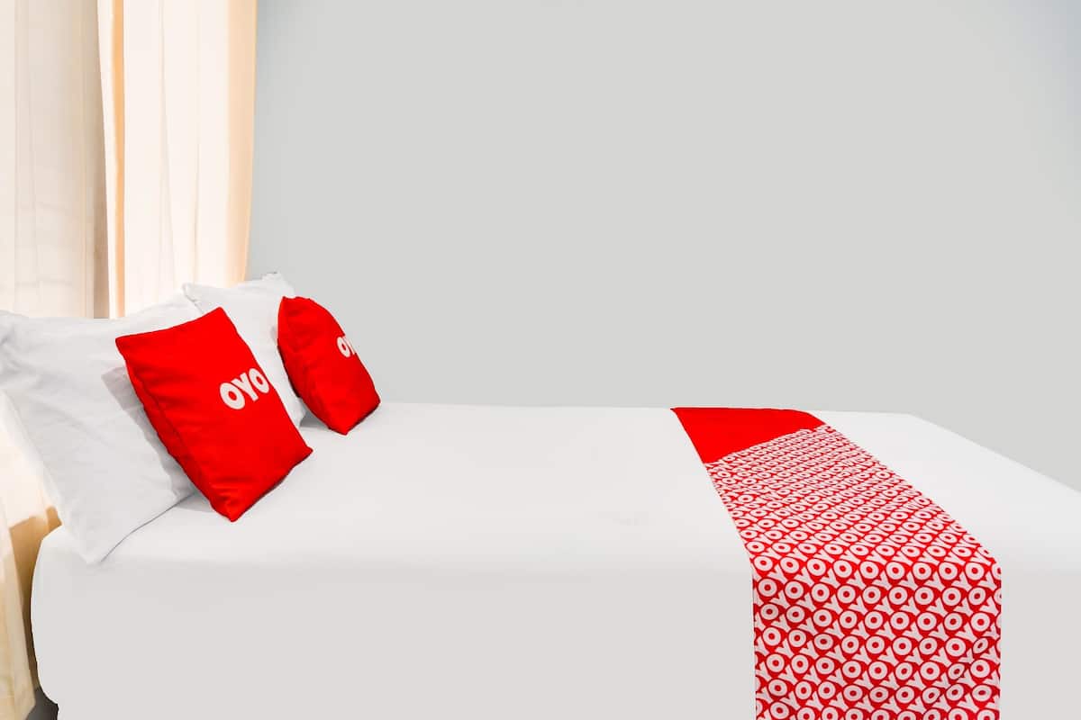 Una habitación de hotel con una cama bien hecha, ropa de cama blanca y almohadones rojos con el logotipo.