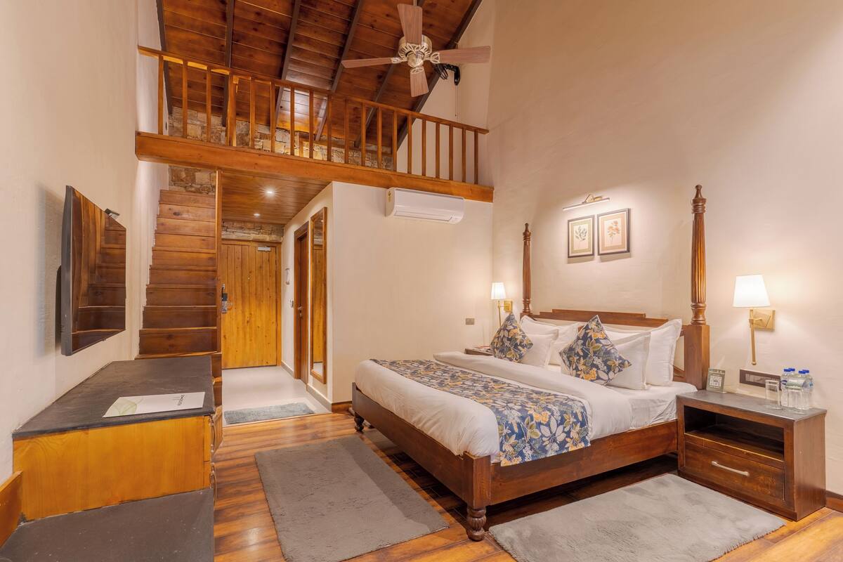 A bedroom with a wooden bed, nightstands, a desk, a ceiling fan, and a staircase leading to an upper level.