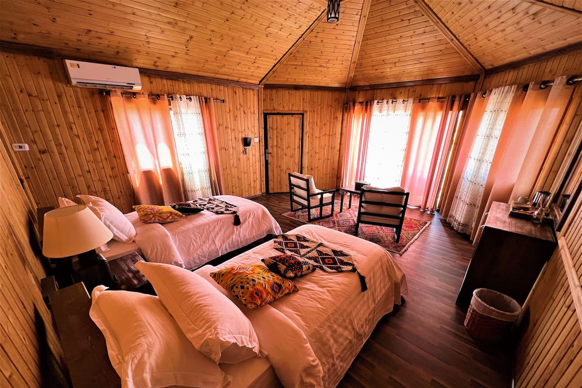 A wooden cabin bedroom with two beds, a desk, and a chair.