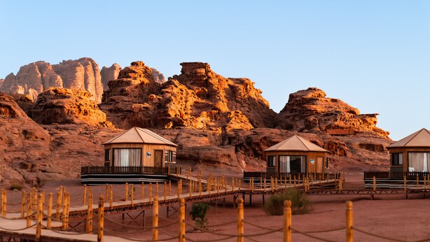 Un resort nel deserto con cabine in legno e un ponte di legno che le collega.