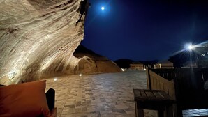 Una veduta interna di una struttura a forma di grotta, con un letto e una panca, illuminata da luci artificiali.