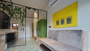 Un intérieur moderne avec un sol à motifs géométriques, un canapé gris, un mur d’accent jaune et une cloison verte.