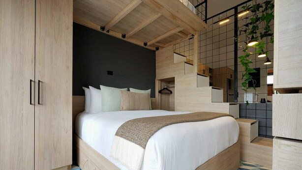 Une chambre moderne avec un grand lit, une armoire en bois et un coin cuisine visible grâce à un espace ouvert.