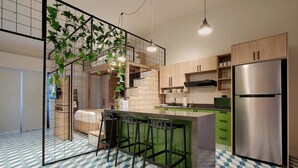Une cuisine moderne dotée d’un coin bar, de tabourets de bar verts, d’un réfrigérateur en acier inoxydable et d’un sol carrelé orné d’un motif géométrique.