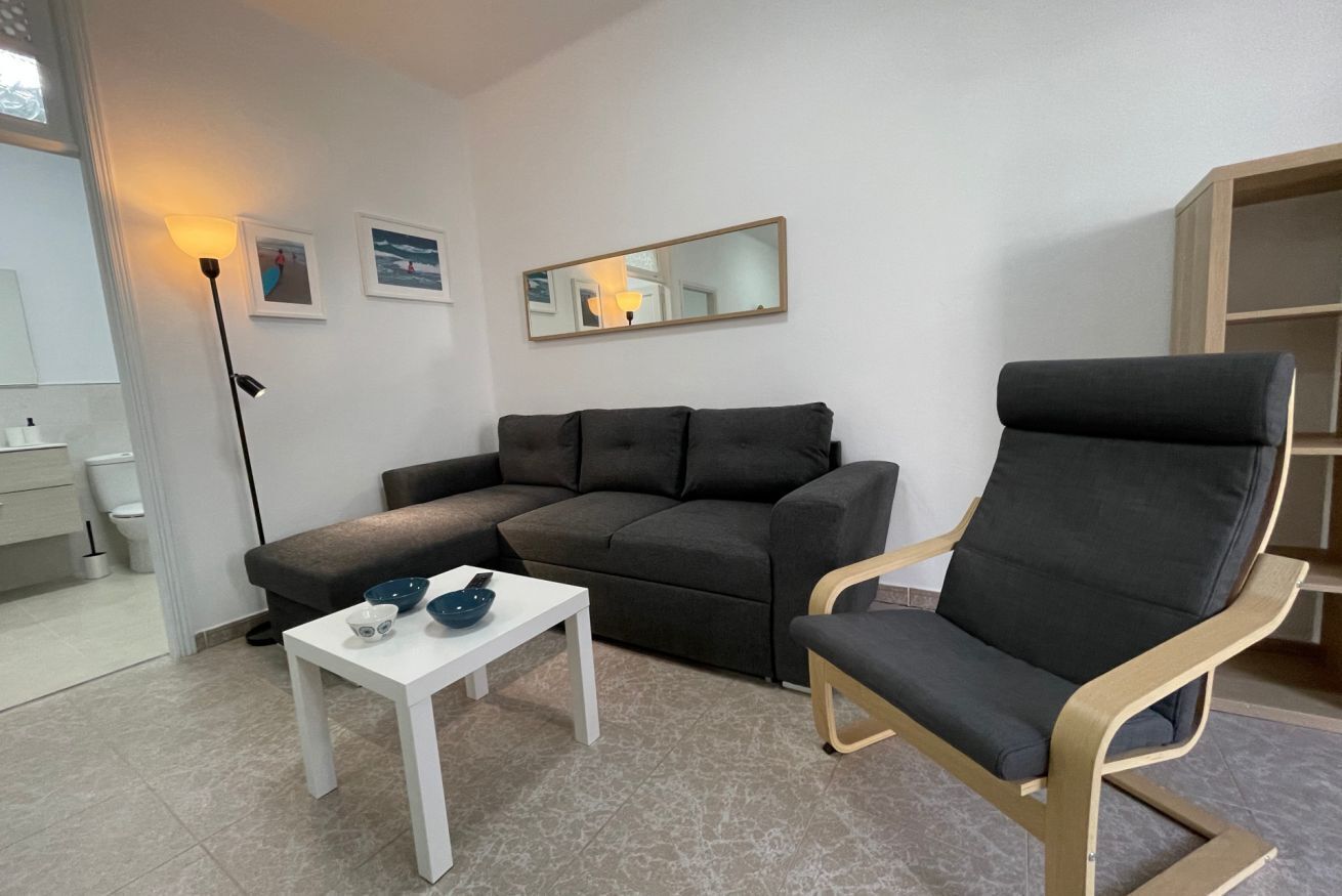 En moderne stue med en grå sofa, et hvidt sofabord og en grå lænestol. Der er et spejl på væggen og en gulvlampe.