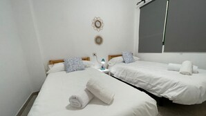 Et hotelværelse med to senge, et natbord med lampe og et stort vindue med persienner.