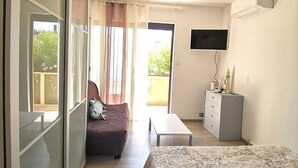 A bedroom with a bed, a TV, a dresser, and a balcony with curtains.