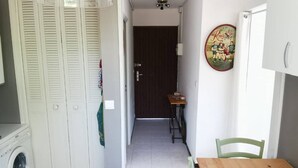 A narrow hallway with a washing machine, a wooden table, and a door leading to another room.