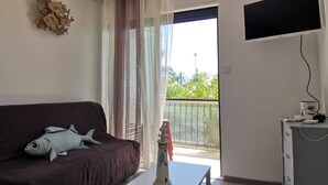 A room with a brown sofa, a fish decoration, a TV mounted on the wall, and a balcony with a railing.