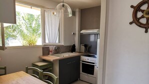 A compact kitchen with a wooden table, a sink, a stove, and a window with curtains.