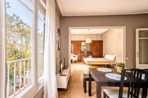 A room with a large window, a dining table with chairs, a bed, and a small kitchen area. - The Collection - Sants Estacio 4BD for 8 Guests (Barcelona)
