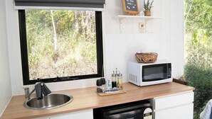 Une cuisine compacte équipée d’un évier, d’un four à micro-ondes et d’une petite étagère sur laquelle est posé un panneau d’accueil.