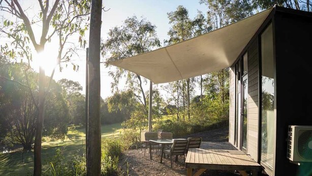 Une terrasse en bois avec des meubles d’extérieur, un grand auvent et un bâtiment aux murs de verre.