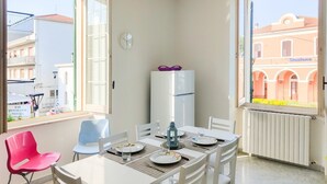A dining area with a table set for four, a refrigerator, and a window with a view of buildings. - Bordopineta Center - Central and bright apartment (Pineto)