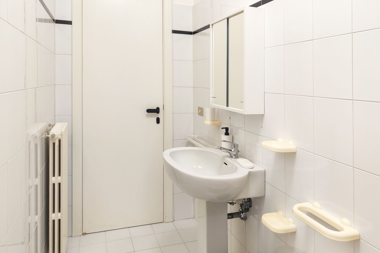 A bathroom with a white sink, a mirror, and a toilet with a grab bar.
