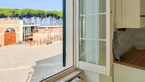 A room with a large window overlooking a courtyard with a fountain, a bike, and a building with trees in the background. - Bordopineta Center - Central and bright apartment (Pineto)