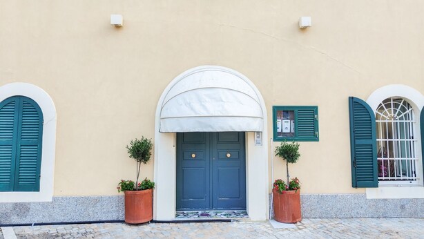 A building facade with a central blue door, flanked by two potted plants and a white awning. - Bordopineta Center - Central and bright apartment (Pineto)