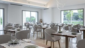 Un comedor moderno con varias mesas y sillas, amplias ventanas que ofrecen vistas a la vegetación exterior.