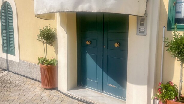 Ein Gebäudeeingang mit weißem Markisenbalkon, einer grünen Tür und einem Blumentopf.