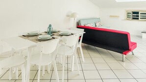Ein Essbereich mit einem weißen Tisch, gedeckt für vier Personen, weißen Stühlen und einer rot-schwarz gestreiften Bank.