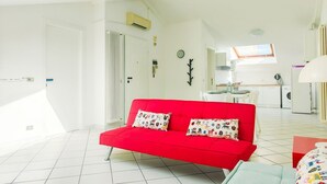 Ein helles Wohnzimmer mit einem roten Sofa, gefliestem Boden und einer Küche im Hintergrund.