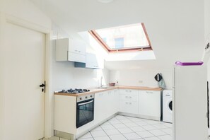 A compact kitchen with a skylight, white cabinets, a stove, and a washing machine. - Homiday - Bordopineta Center - Bright and spacious apartment on the second floor (Pineto)