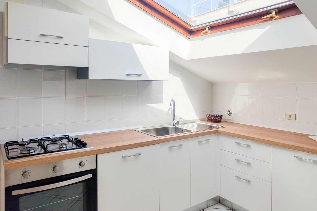 Une cuisine moderne avec des meubles blancs, un plan de travail en bois, une cuisinière à gaz et une lucarne au-dessus de l’évier.