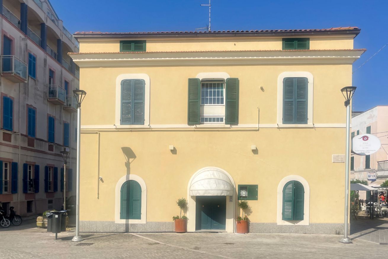 A building with a yellow facade, green shutters, and a central arched entrance.