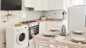 Una cocina moderna con armarios blancos, horno empotrado, lavadora y comedor con mesa dispuesta para dos.