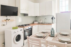Une cuisine moderne avec des meubles blancs, un four encastré, un lave-linge et un coin repas avec une table dressée pour deux personnes.