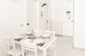 Un coin repas avec une table blanche dressée pour quatre personnes, des chaises blanches et une lanterne bleu clair.