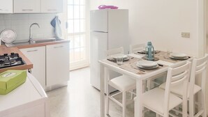 Una cocina moderna con armarios blancos, cocina a gas, refrigerador y un comedor con sillas blancas y una mesa para dos.