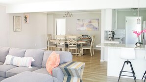 Una sala de estar moderna con un sofá gris, un comedor con sillas de madera y una isla de cocina con un taburete.